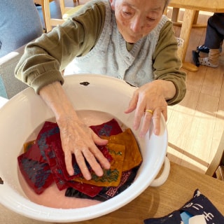 洗面器に入った水にタオルを浸すお年寄りの女性